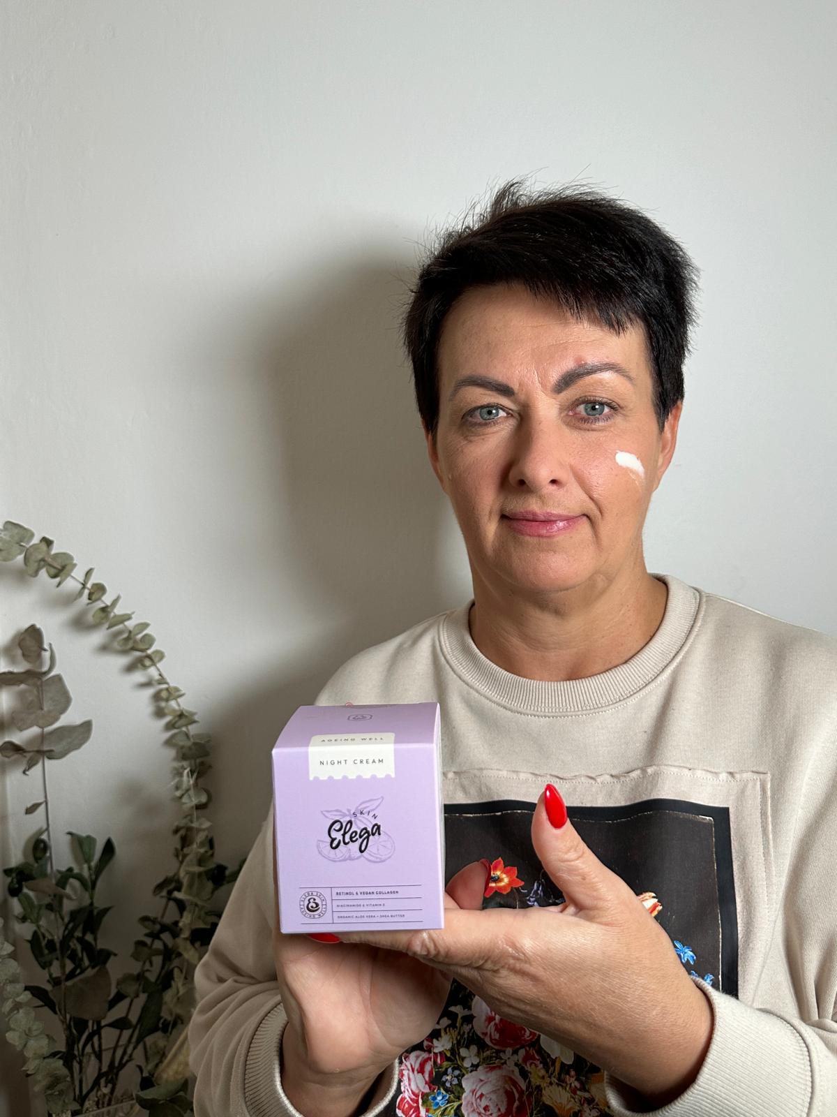 Person holding a box of night cream against a plain background.